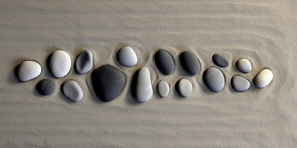 A row of smooth pebbles of different sizes and shades, arranged on raked sand